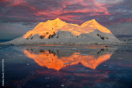 Mountain with red orange top light up by midnight sun with reflection in the sea in Antarctica 