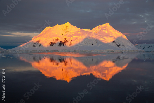 Mountain with red orange top light up by midnight sun with reflection in the sea in Antarctica 