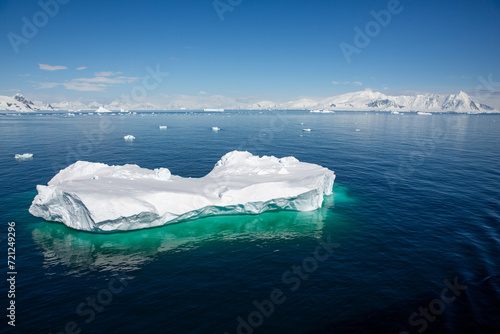 Floating iceberg with clear visible part under the water  glacier in the background and blue sky