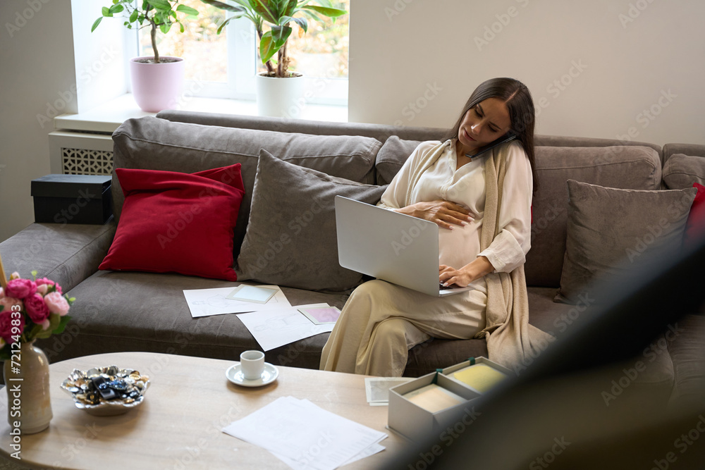 Pregnant female sits in relaxation area with laptop and mobile phone Pregnant female sits in relaxation area with laptop and mobile phone