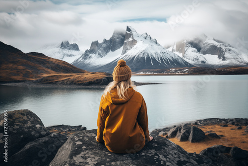 Rear view of a female traveler sitting on a rock near a lake looking at the mountains