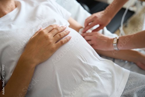 Selective focus of pregnant woman belly while nurse put drop counter to her © Svitlana