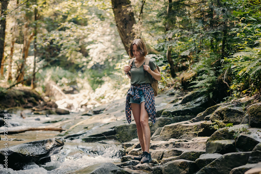 Naklejka premium Full length of young female traveler with backpack walking by the stones along the mountain river