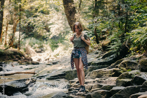 Full length of young female traveler with backpack walking by the stones along the mountain river