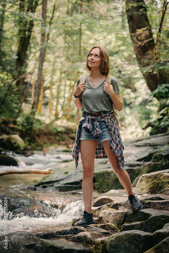 Beautiful young female traveler with backpack walking by the stones along the mountain river