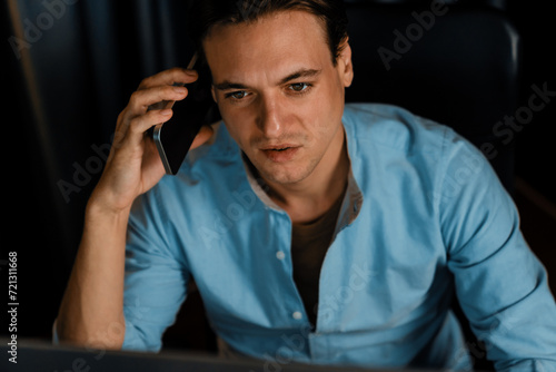 Smart businessman calling with smartphone for consulting business paragraph dynamic database marketing analysis plan surrounded paper sheet and pc monitor report at home office at night. Pecuniary.