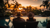 Rear view of a young couple sitting by the swimming pool at sunset