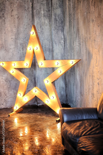 Decorative lighting star-shaped sign in a loft interior.Studio decor with light bulbs with retro style dark leather sofa