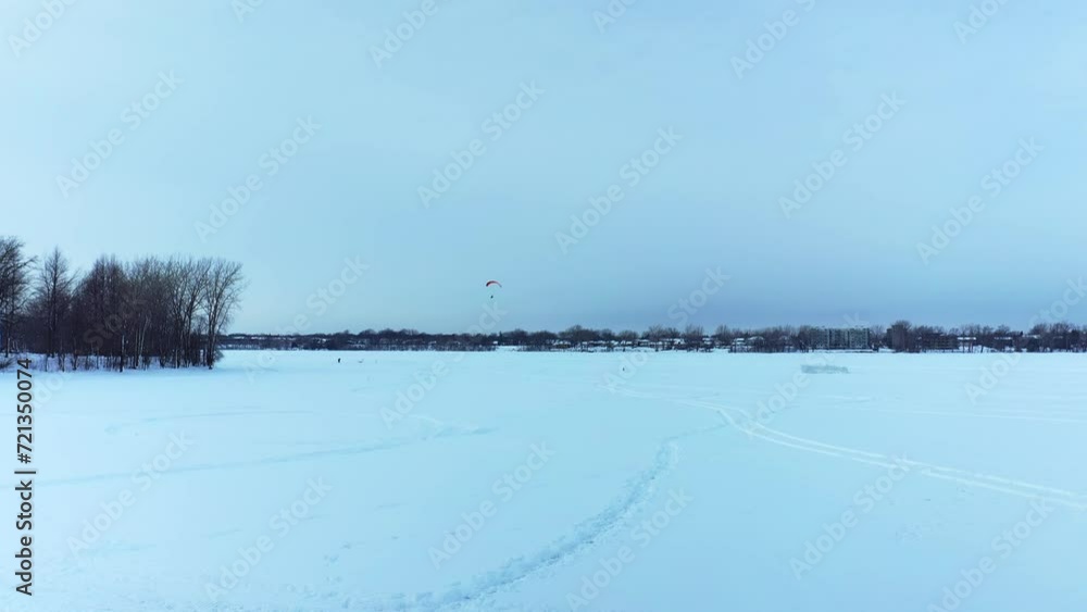 Almost still aerial drone shot showing the fort made of ice, people playing on the frozen lake and a motorized deltaplane flying over the river at Berge-des-goelands in Laval-Ouest-24fps Almost still aerial drone shot showing the fort made of ice, people playing on the frozen lake and a motorized deltaplane flying over the river at Berge-des-goelands in Laval-Ouest-24fps