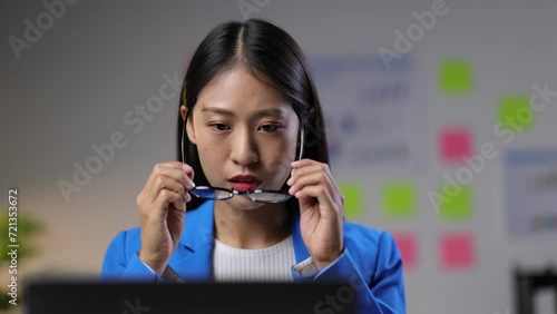 A nearsighted businesswoman wears glasses while working in the office. Attractive young Asian woman working happily on laptop in office.