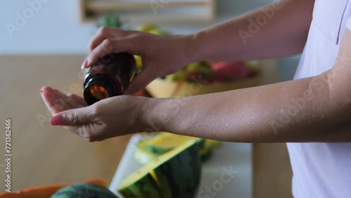 Close-up of woman taking medicine from pill bottle by exotic tropical fruits, slow motion. Selective focus. Vitamins, nutritional supplements and healthy lifestyle concept photo