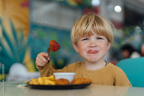 happy boy with blond hair eats fries and nuggets in restaurant