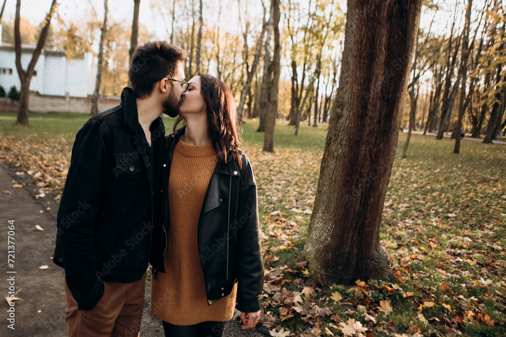 Heterosexual caucasian young loving couple walking outside in the city park in sunny weather, hugging smiling kissing laughing spending time together. Autumn, fall season, orange yellow red maple leav Heterosexual caucasian young loving couple walking outside in the city park in sunny weather, hugging smiling kissing laughing spending time together. Autumn, fall season, orange yellow red maple leav