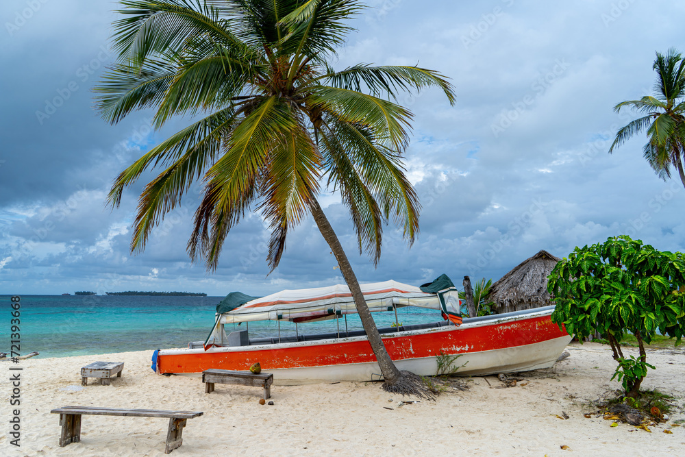 Red boat on sand beach shore behind single palm tree and blue caribbean water in background normal exposure