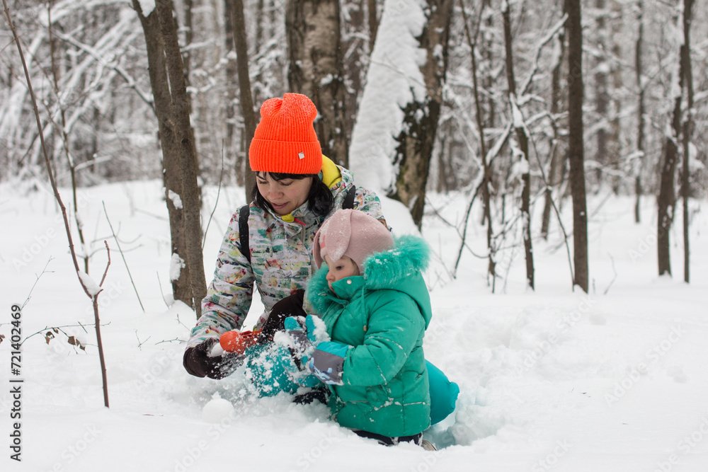 Mom and daughter are playing in the snow and making a snowman. Winter walk in the fores Mom and daughter are playing in the snow and making a snowman. Winter walk in the fores