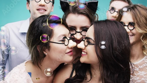 Happy people, bubbles and party with glasses, celebration and eskimo kiss with friends. Dancing, photobooth and bonding together with men, woman and social gathering on studio background for fun photo