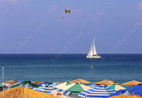 Multi-colored beach umbrellas against the background of a blue sea sky and a yacht.