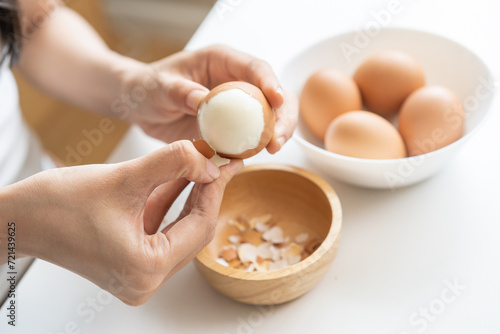 Protein in food, keto diet asian young woman hand peeling, shelling chicken boiled egg, prepares ingredient for breakfast meal on table at home. Removing egg shell, cleaning egg, health care concept. photo