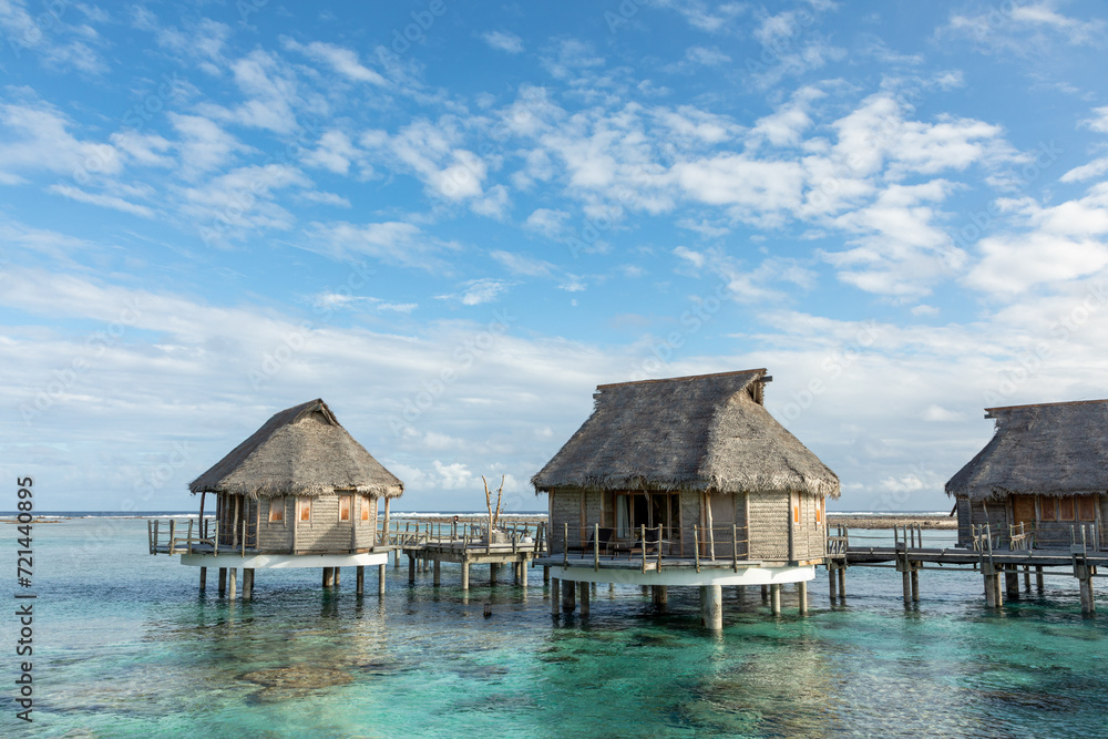 French Polynesia Tikehau atoll with pink coral reef lagoon and two overwater bungalows under cloudy sky. French Polynesia Tikehau atoll with pink coral reef lagoon and two overwater bungalows under cloudy sky.