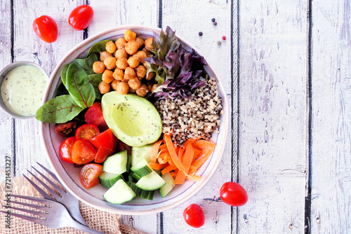 Healthy homemade salad bowl with avocado, chickpeas, quinoa and vegetables. Top down view table scene on a white wood background.