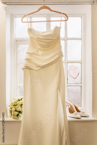 Beautiful bridal fashionable wedding white high heels shoes  dress  and a bridal bouquet near a window at home.  Wedding