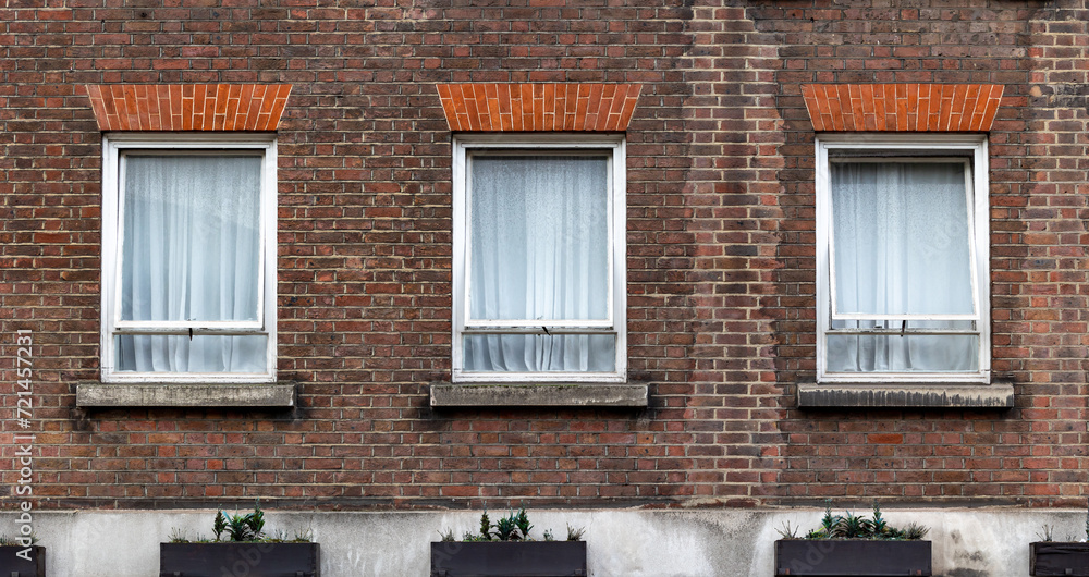 three aligned classic white windows of typical london architecture with red brick wall