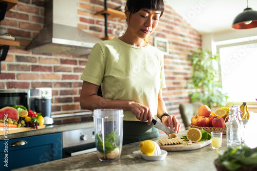 Young asian woman preparing healthy smoothie in home kitchen photo