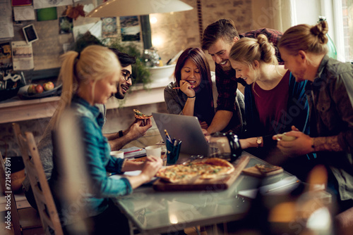 Friends enjoying pizza and looking at laptop together at home photo