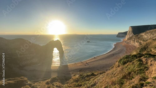The sun goes down on the Jurassic coast and Durdle Door in Dorset with Seak Pink Trift growing on the top of the cliff in the foreground. Durdle Door, Dorset, Jurassic Coast, England, UK photo