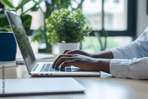 Close-up of hands of black person working and typing on laptop in beautiful office