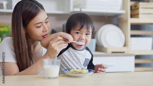 Young Asian mother support little boy to eat food in kitchen by help to suport hold spoon for the child. photo