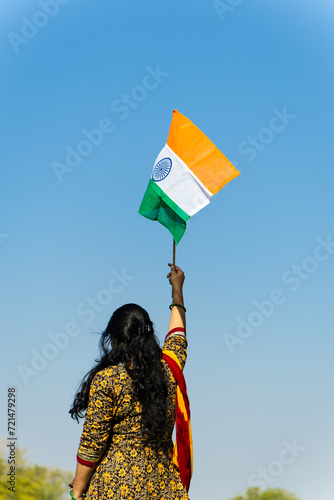 young indian girl holding the indian tricolor national flag waving with bright blue sky at day