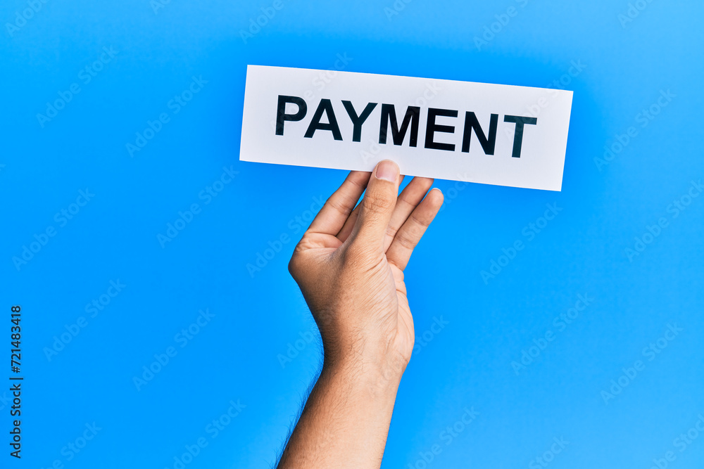 Hand of caucasian man holding paper with payment word over isolated blue background Hand of caucasian man holding paper with payment word over isolated blue background