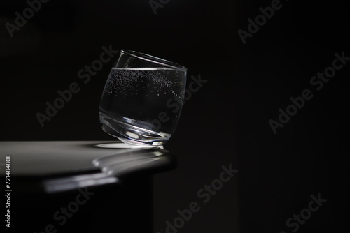 Bujająca się na granicy krawędzi szklanka wypełniona kryształową wodą. Kontrapunkt dla ciemnego tła. To metafora równowagi i balansu.
