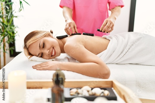 Young caucasian woman lying on table having back massage using hot stones at beauty salon