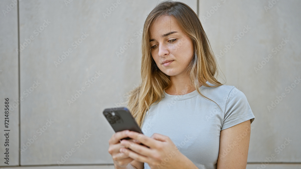 Cool, young blonde woman in casual fashion, seriously engrossed in her smartphone outside on urban city street. concentrated young caucasian female texting, engrossed in her online lifestyle. Cool, young blonde woman in casual fashion, seriously engrossed in her smartphone outside on urban city street. concentrated young caucasian female texting, engrossed in her online lifestyle.