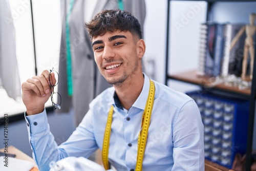 Young hispanic man tailor smiling confident sitting on table at tailor shop photo