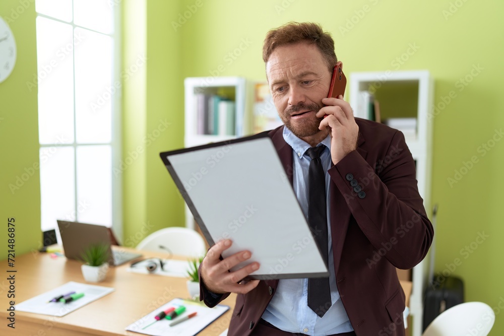 Middle age man business worker talking on smartphone reading document at office Middle age man business worker talking on smartphone reading document at office