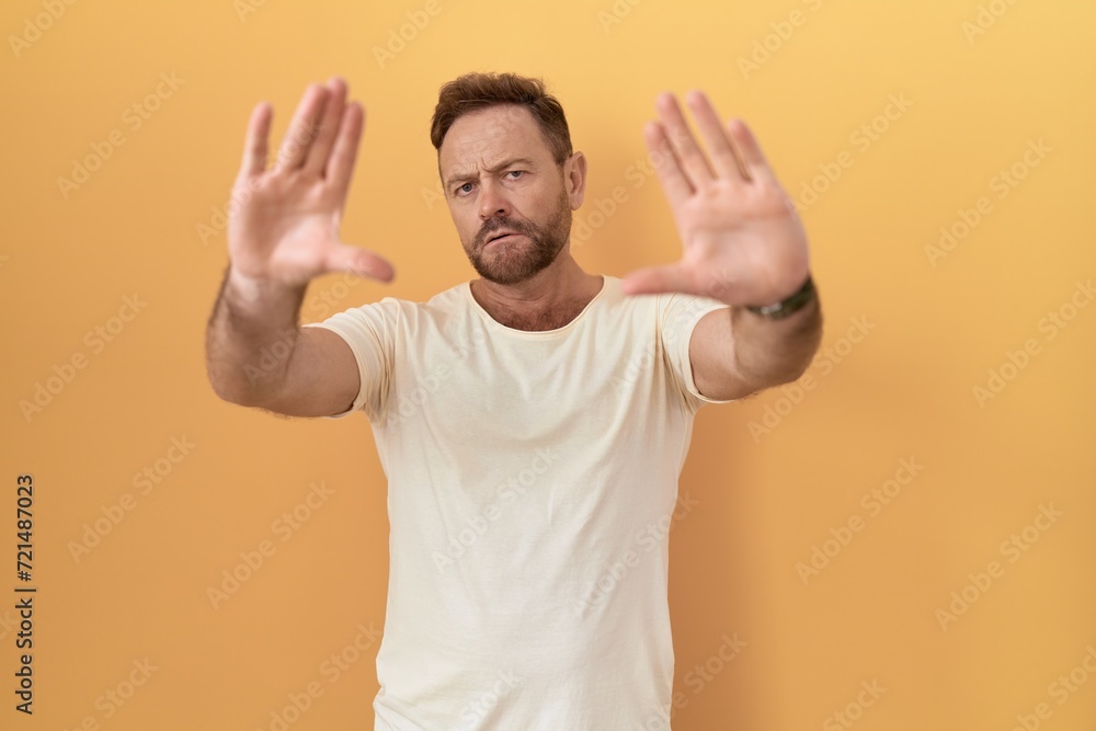 Middle age man with beard standing over yellow background doing frame using hands palms and fingers, camera perspective Middle age man with beard standing over yellow background doing frame using hands palms and fingers, camera perspective