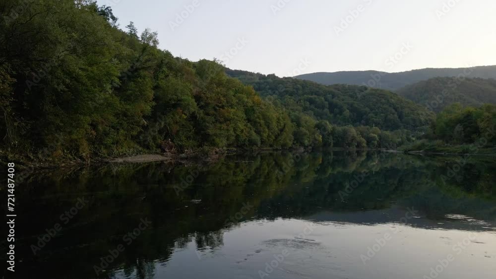 Drone flies over river towards shore full of green lush bushes and trees Drone flies over river towards shore full of green lush bushes and trees
