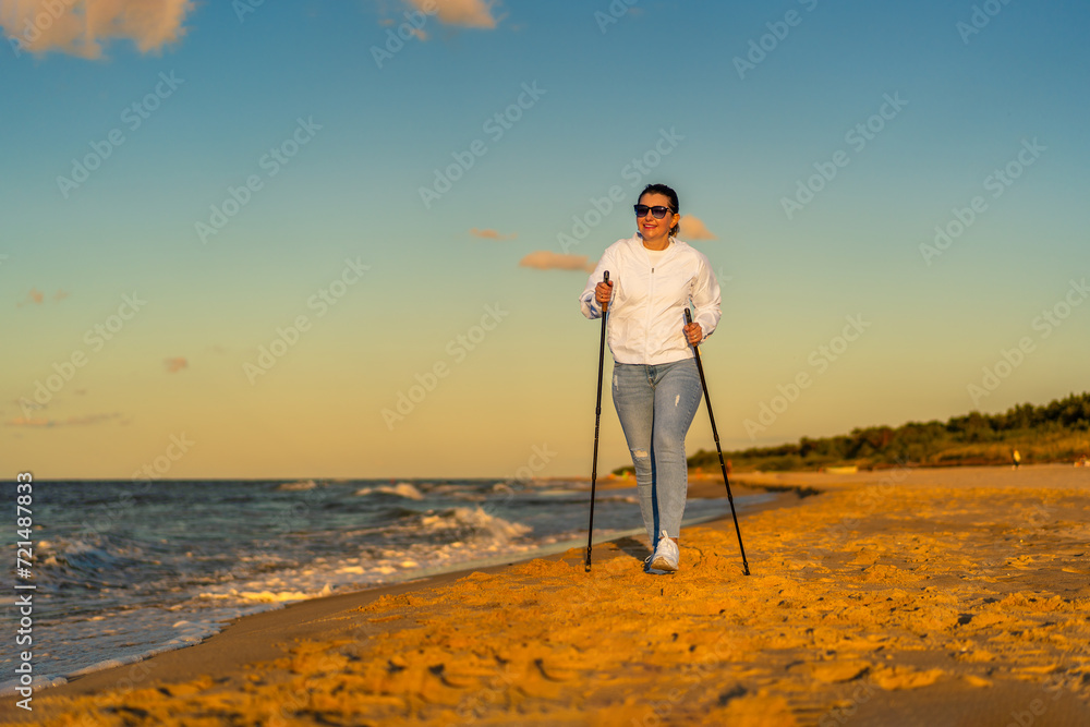 Nordic walking - beautiful woman exercising on beach at sunset
