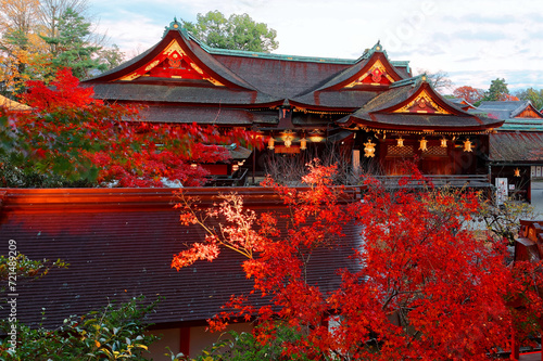Beautiful autumn scenery of maple trees by majestic traditional Japanese architectures in Kitano Tenmangu, a famous Shinto Shrine (Jinja) in Kyoto, Japan, with fiery foliage lighted up before dusk