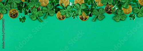 St Patricks Day top border of  shiny shamrocks and gold coins. Top view over a green banner background with copy space.