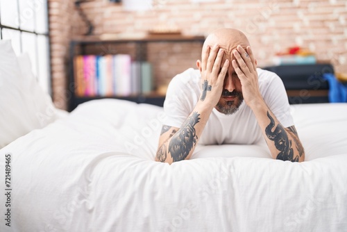 Young bald man stressed lying on bed at bedroom