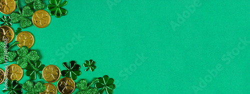 St Patricks Day corner border of  shiny shamrocks and gold coins. Top view over a green banner background with copy space.