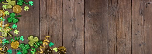 St Patricks Day corner border of green shamrocks, gold coins and ribbon. Top down view over a rustic dark wood banner background with copy space.