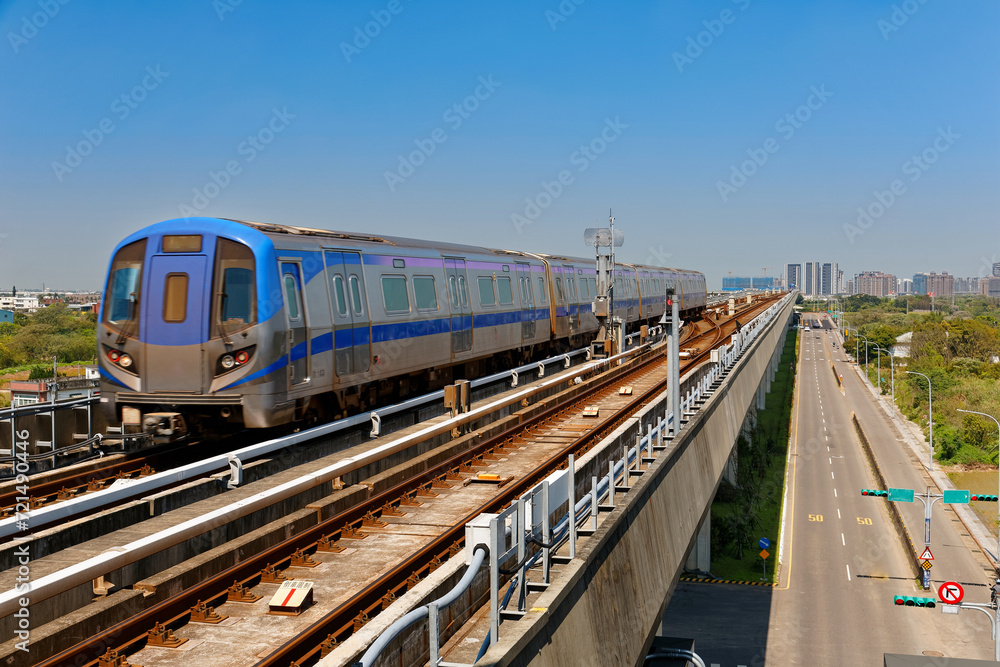Naklejka premium Scenic view of a metro train traveling on elevated rails of Taoyuan Mass Rapid Transit System (International Airport MRT System) under blue clear sky in Zhongli, New Taipei City, Taiwan