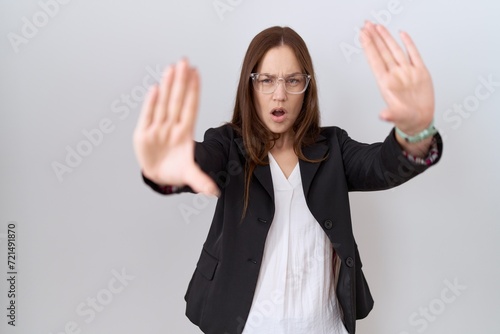 Beautiful brunette woman wearing business jacket and glasses doing stop gesture with hands palms, angry and frustration expression