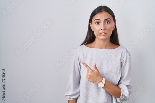 Young hispanic woman standing over white background pointing aside worried and nervous with forefinger, concerned and surprised expression
