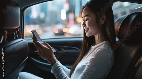 Woman is sitting in the backseat of a car, looking at her smartphone with a smile © MP Studio